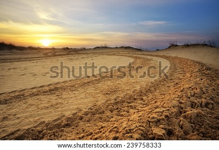 Motocross and auto sport track with sunset sky background. Wheel tracks on sand
