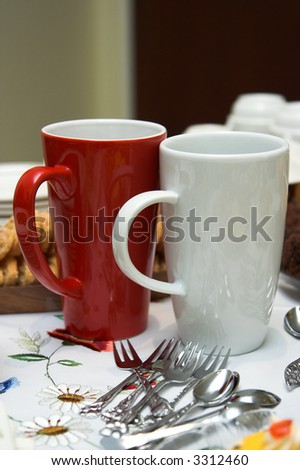 Two tall mugs standing on a coffee table at a tea-party. Cake forks and spoons are lying on the table. The mugs are red and white in color