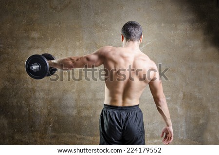 Young man training shoulder and back muscles exercises in old gym
