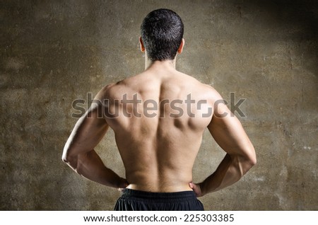 Posing strong young man with arms on hip on dirty wall background