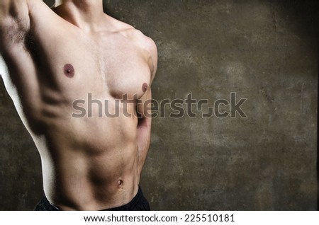 Close up image of young man fitness gym torso with dramatic light on dirty wall background with copy space.