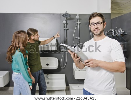 Sales clerk looking catalog at plumbing store with blurred couple looking in the background