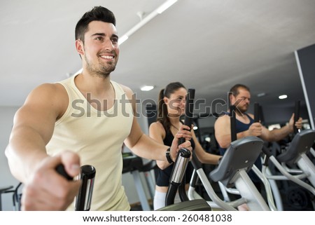 Active people at gym in elliptical bike, smiling man in focus.