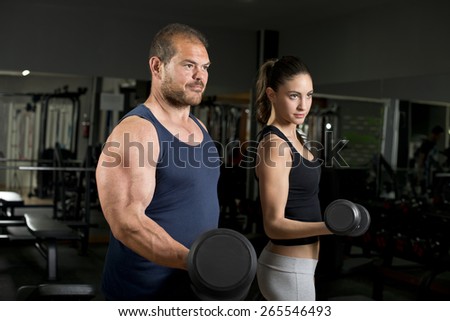 Strong coach and beauty girl at gym training biceps