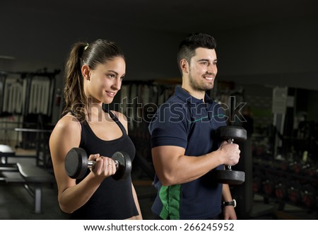Beauty young woman training lifting weights at gym. Coach is blurred in second frame.