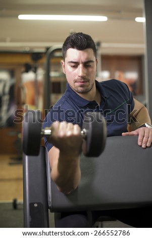 Young man training biceps at gym in curl bench.
