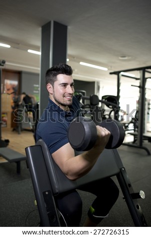 Young man training biceps muscle at gym.