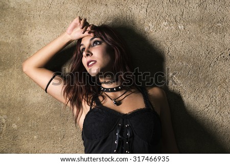 Young woman with gothic and heavy metal style and spiked collar posing on dirty wall background
