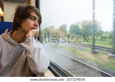 Bored young man, staring out the train window on a rainy, grey and dull day