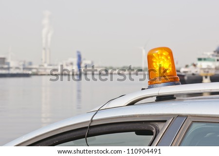 Orange flashing light on top of a support and services vehicle in an industrial harbor