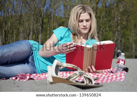 Attractive blonde woman reading a book on a sandy beach on a beautiful, sunny, spring day.