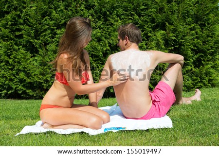 A young woman applying a suntan lotion on a man's back while sunbathing in a back yard