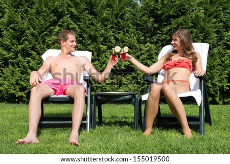 A young couple sunbathing in a back yard and toasting with tropical drinks