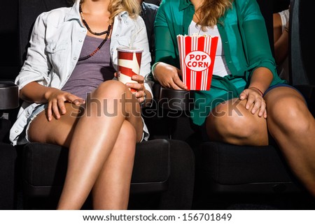 Midsection of young women with popcorn and soda sitting in cinema theater