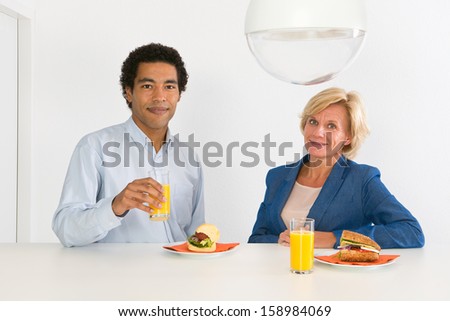 Two coworkers during lunch at a counter in their office, with fresh orange juice and healthy sandwiches