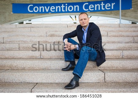 Businessman is attending a convention and sits in front of the entrance of the convention center