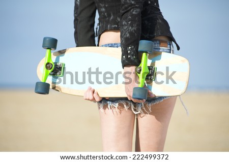 Fashionale woman in hot pants and designer jacket holding a skateboard behind her back