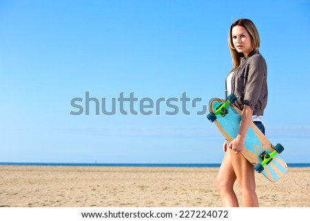 Young, athletic, woman,  with long bronzed legs, walking on a deserted beach, holding a skateboard
