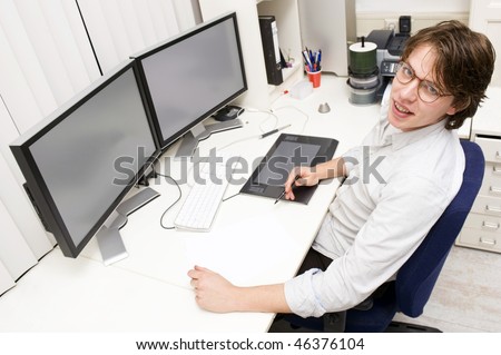 A designer at work behind two monitors, looking up at the camera