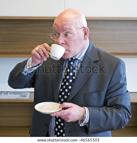 A senior manager sipping coffee and looking up from behind his cup at what is going on around him