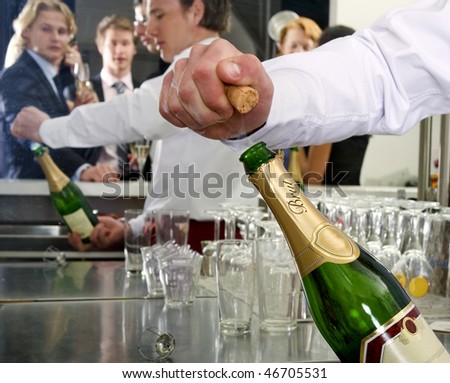 A bar man opening a bottle of champagne behind a bar, with several people reflected in the mirror behind him
