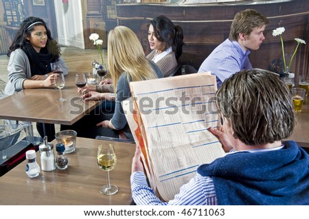 A man reading a financial paper with several people at different tables in the same cafe