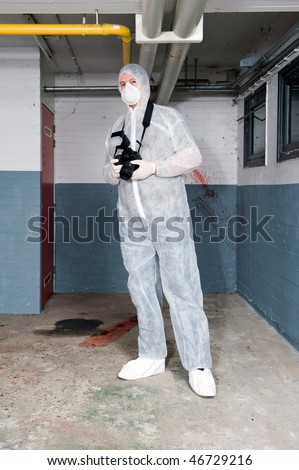 Forensics expert, dressed in a white protective suit, mask and shoe covers, carrying a camera, posing in a basement