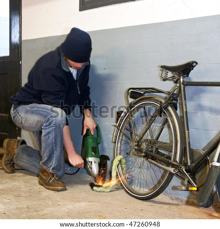 Bicycle thief busy breaking the lock with a portable grinding machine