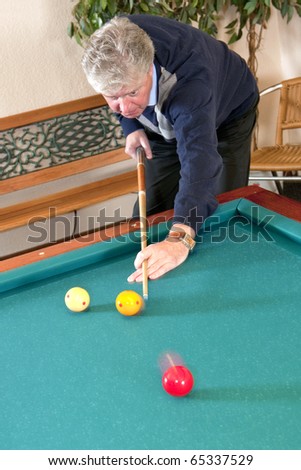 Senior man playing carambole billiards - slight motion blur in the red and yellow billiard balls