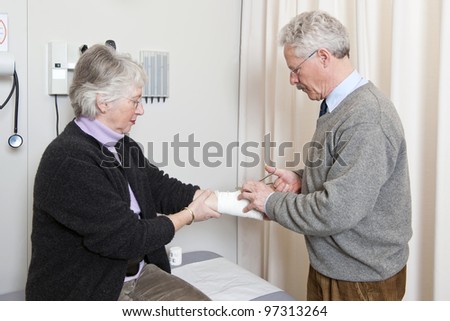 Doctor cutting off the bandage on an elderly woman\'s arm with scissors in a general medical practice