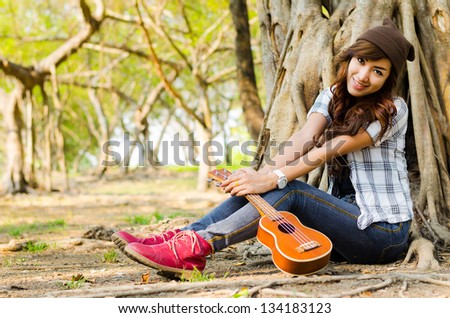 beautiful lady sitting under the tree with ukulele