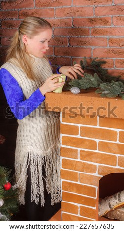 Beautiful woman standing by fireplace with mug of hot drink