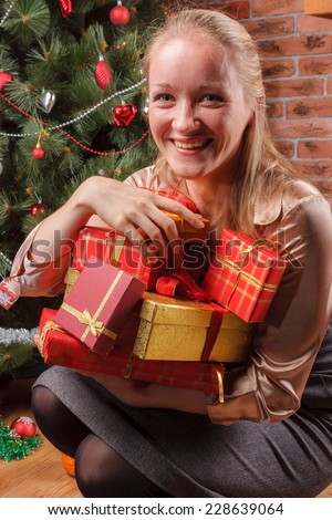 Happy woman sitting under Christmas tree with pile of Christmas presents