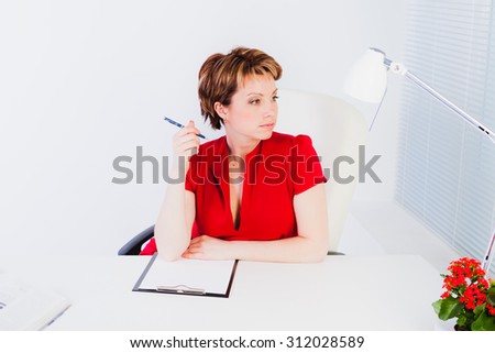 Lovely woman in red dress sitting by desk in white office