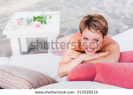 Smiling short-haired woman laying on white sofa in outdoor cafe