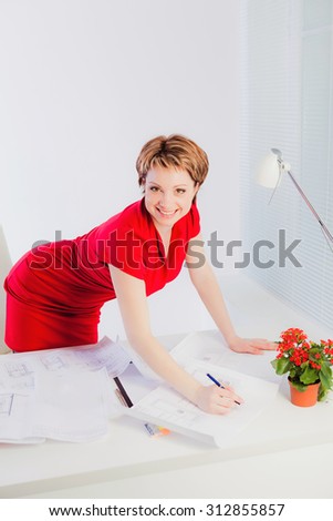 Beautiful woman in red dress standing nearby office desk with papers