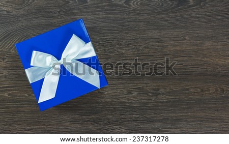 Blue gift box with light blue bow on dark wooden background