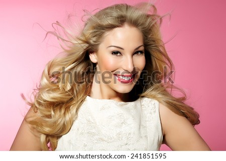 Beautiful woman with long blond hair and nice makeup posing on pink background.
