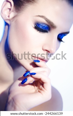 Closeup of a model with blue glitter makeup and manicure. Lighting and model look slightly like 90s style.