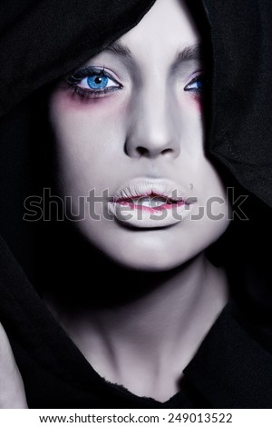 Spooky woman with intense pale face in black cape.