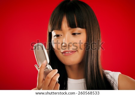 Young Asian girl with mobile phone on red background.