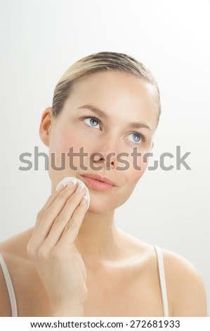 Young beautiful woman cleansing face with toner on cotton disk. Makeup removal in skincare routine.