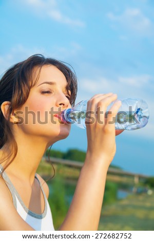 Young woman outdoor against blue sky and Dutch green rural landscape drinking from bottle of mineral water.
