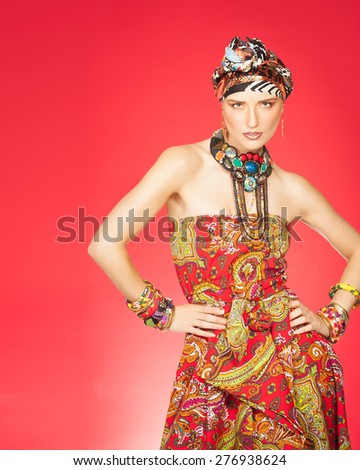 Colorful exotic gypsy style fashion woman wearing red dress and turban over red background.