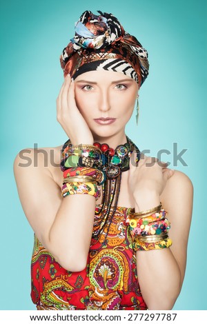Colorful exotic gypsy style fashion woman wearing red dress and turban over cyan background.