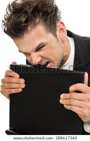 Young Caucasian man angry and desperate biting laptop indoors over white background.
