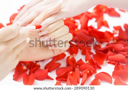 Professional manicure process with red rose petals. Four female hands closeup.