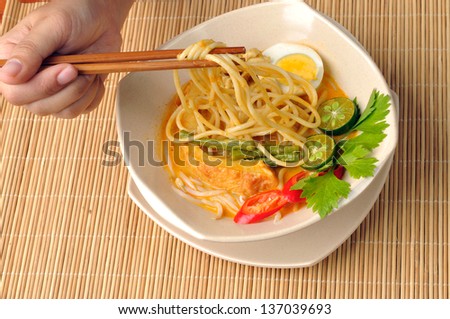 Cropped view of hand holding chopstick to eat curry noodles