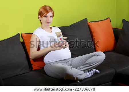 Pregnant woman sitting on sofa and holding a teddy bear