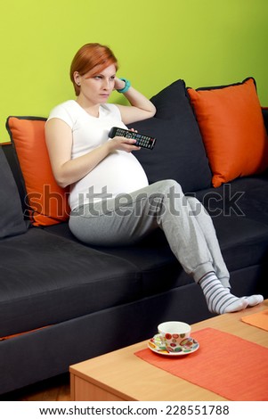Pregnant woman sitting on sofa with TV remote control